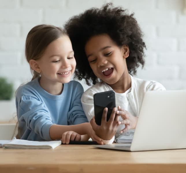 Dua anak tertawa sambil belajar dengan ponsel